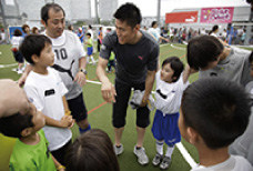 写真：グラウンドで子供達に囲まれて指導している選手